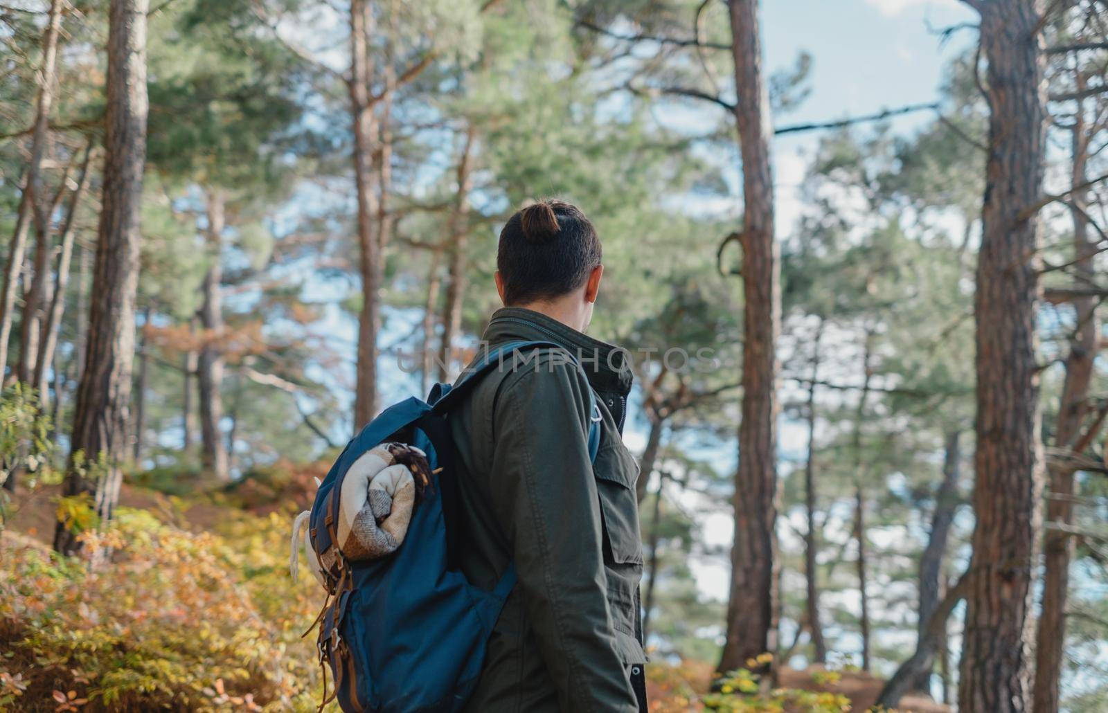 Unrecognizable traveler young man with backpack walking in autumn forest