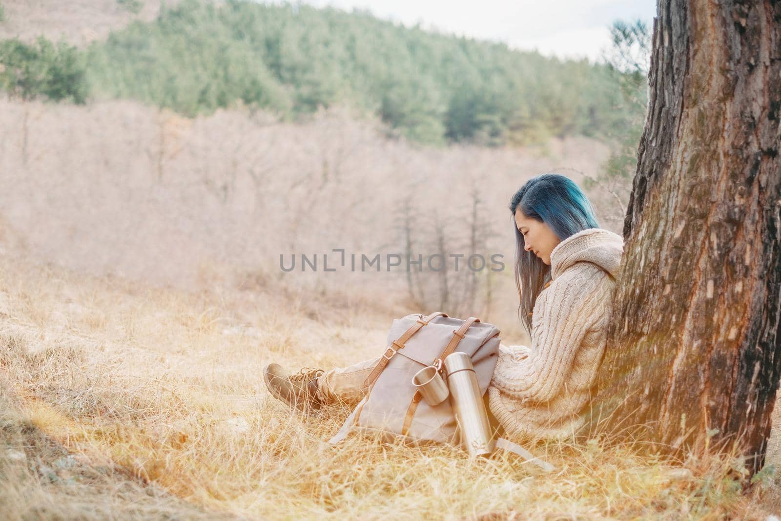 Traveler young woman with backpack and thermos resting near a tree outdoor in sunny day
