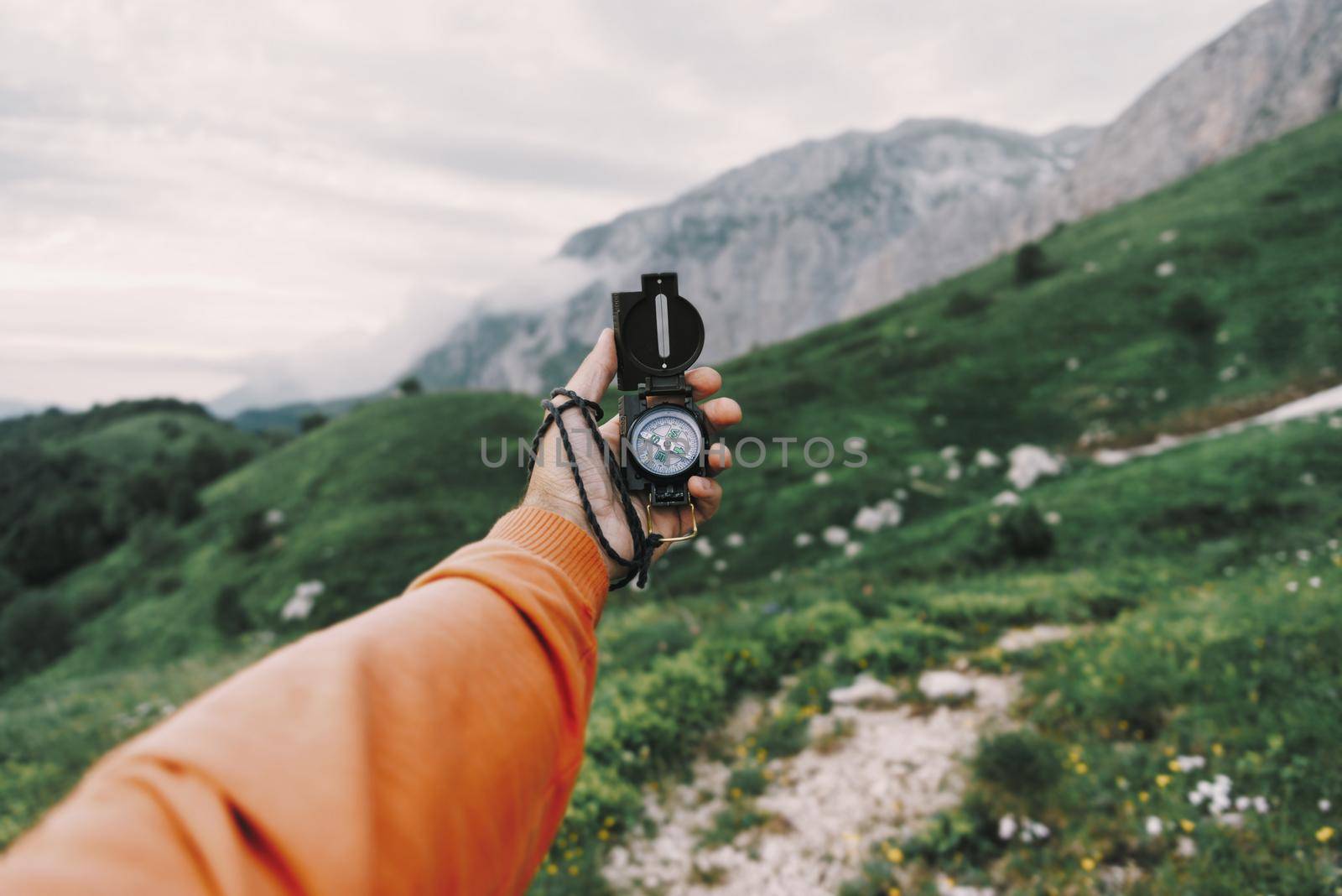 Male explorer searching direction with compass in summer mountains, point of view.