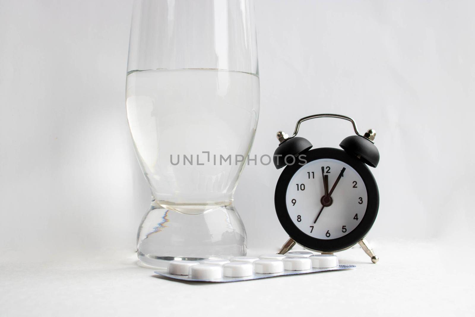 Medical tablets and a glass of water next to the clock on a white background by lapushka62