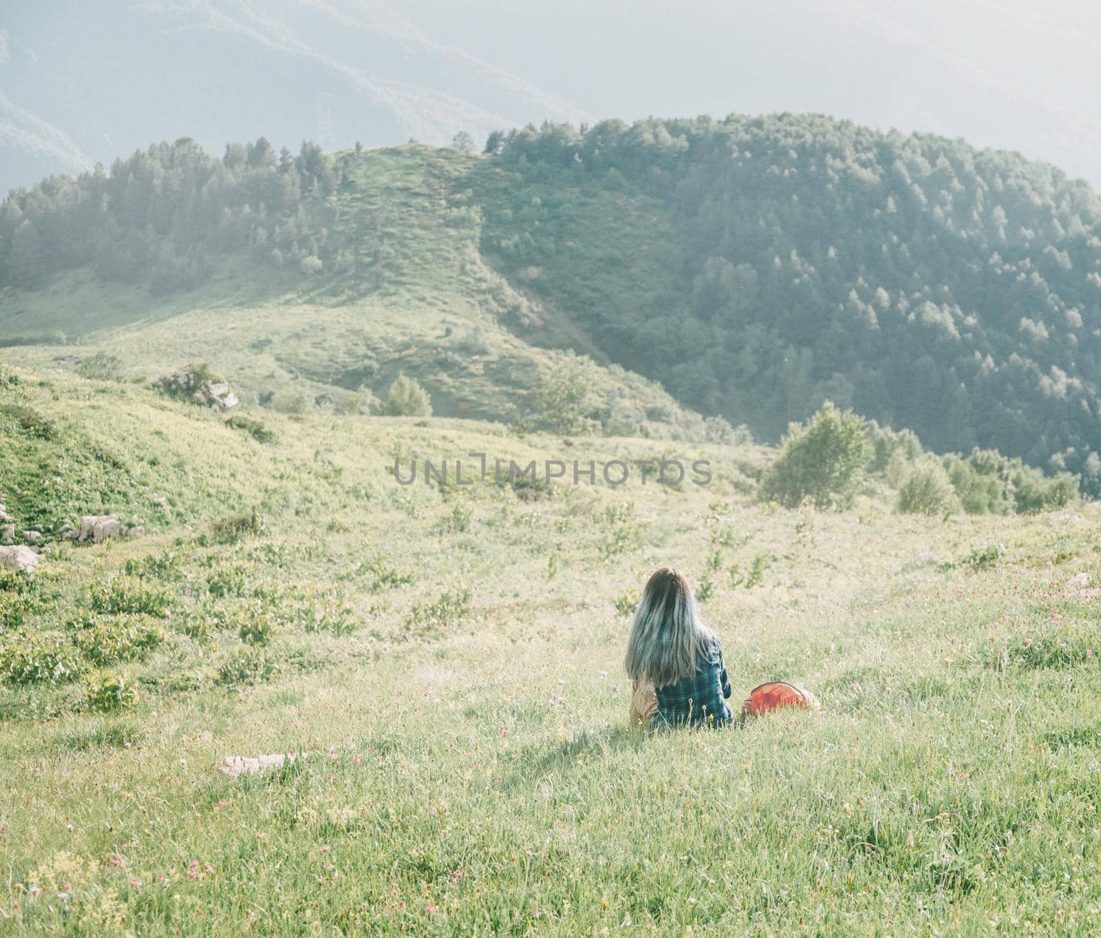 Young woman is resting on summer mountain meadow in sunny day, rear view.
