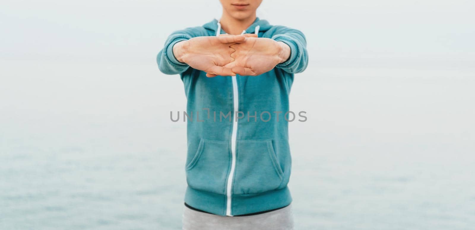 Fitness young woman stretching her hands on background of sea, workout