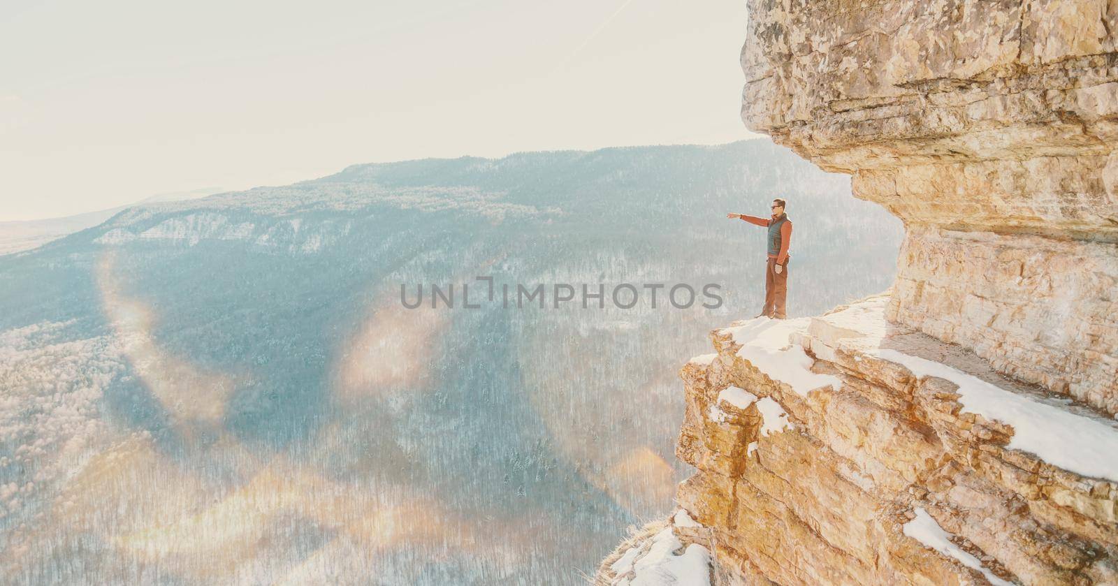 Explorer young man standing on high cliff Eagle shelf and pointing into the distance in winter, Mezmay, Russia. Image with sunlight effect.