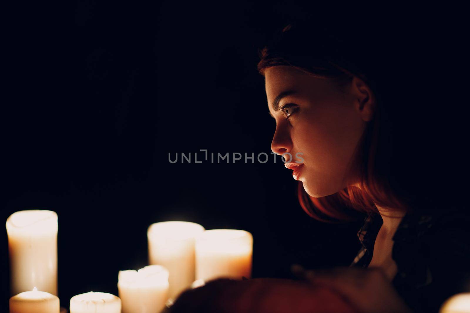 Young woman profile portrait with candles light in darkness. Edge lit face