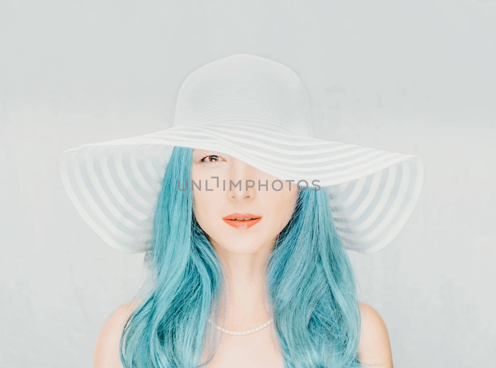 Attractive young woman with blue hair in a hat with wide brim, looking at camera.