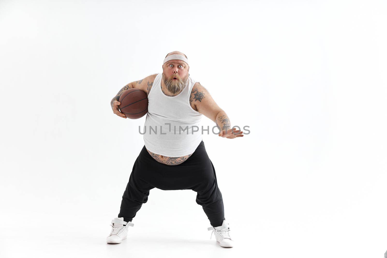 bearded fat caucasian tattoed man with basketball ball in white background. He is funny and happy