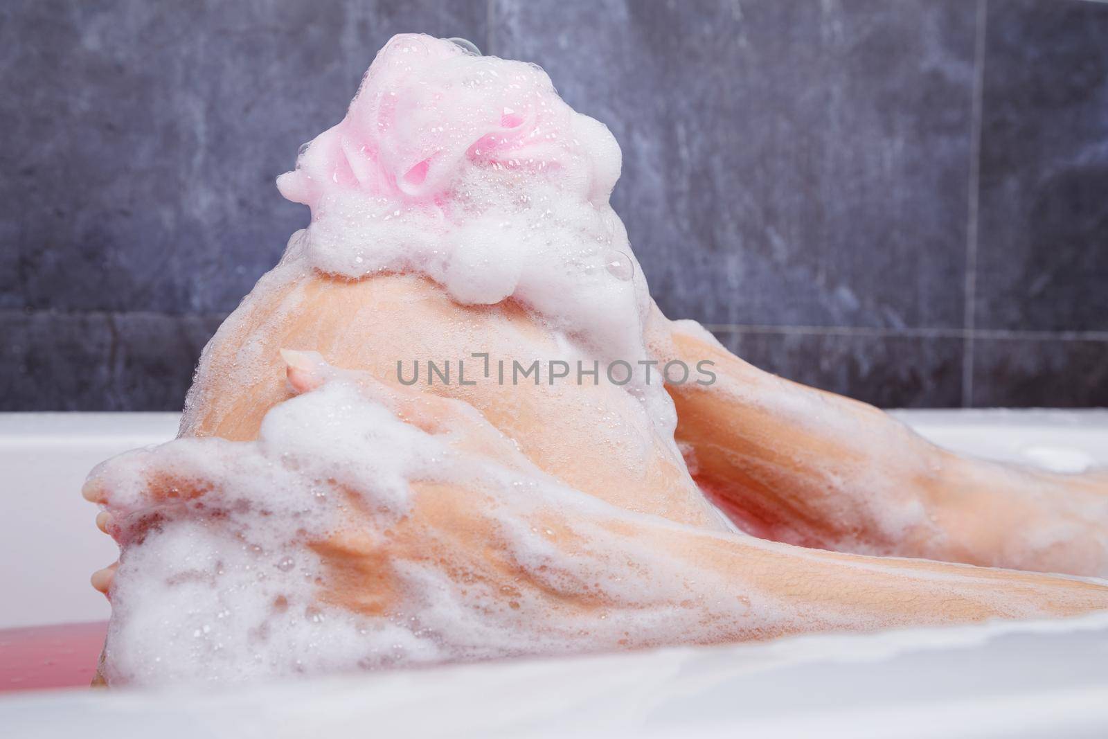 close up of woman washing knee with pink sponge in bathtub in the bathroom