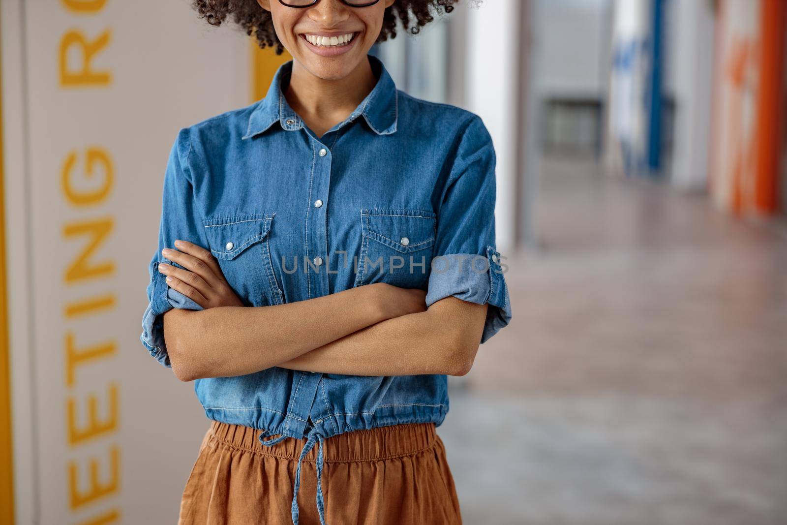 Cropped photo of smiling Afro American lady standing in oofice hall with arms crossed, copy space