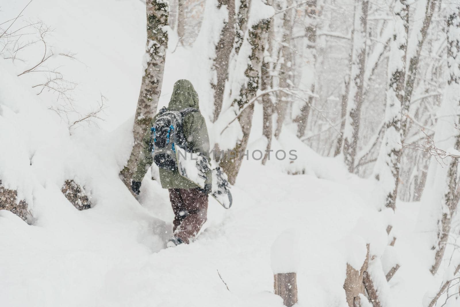 Unrecognizable freerider young man with snowboard walking in winter forest, rear view. Focus on foreground, blurred figure of a man.