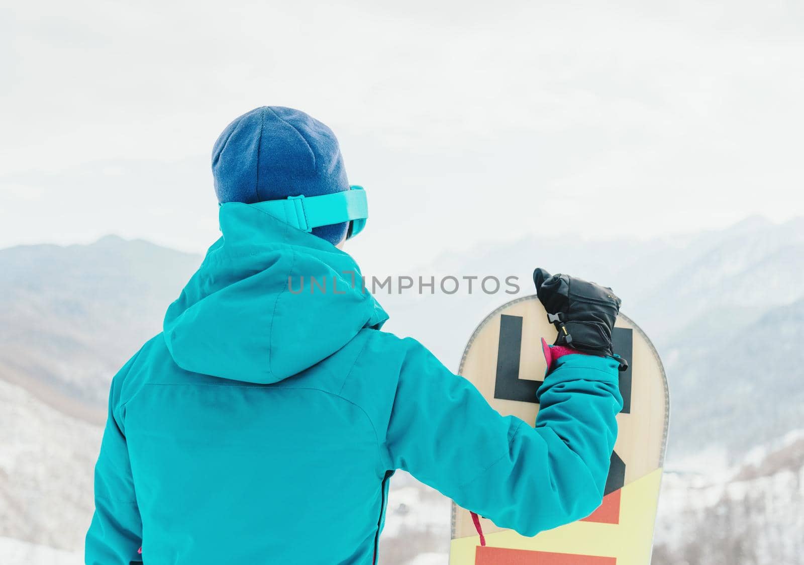 Young woman with snowboard looking at snowy mountains, rear view