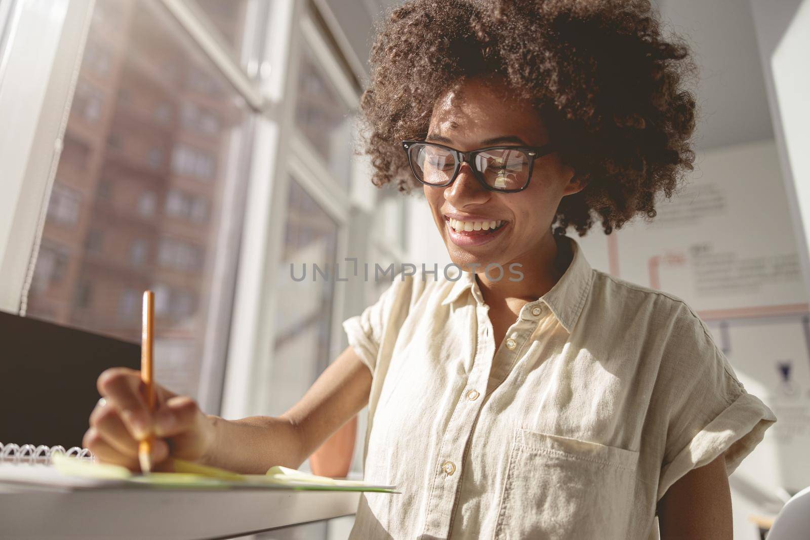 Happy young woman making notes in a notebook at the desk in the office