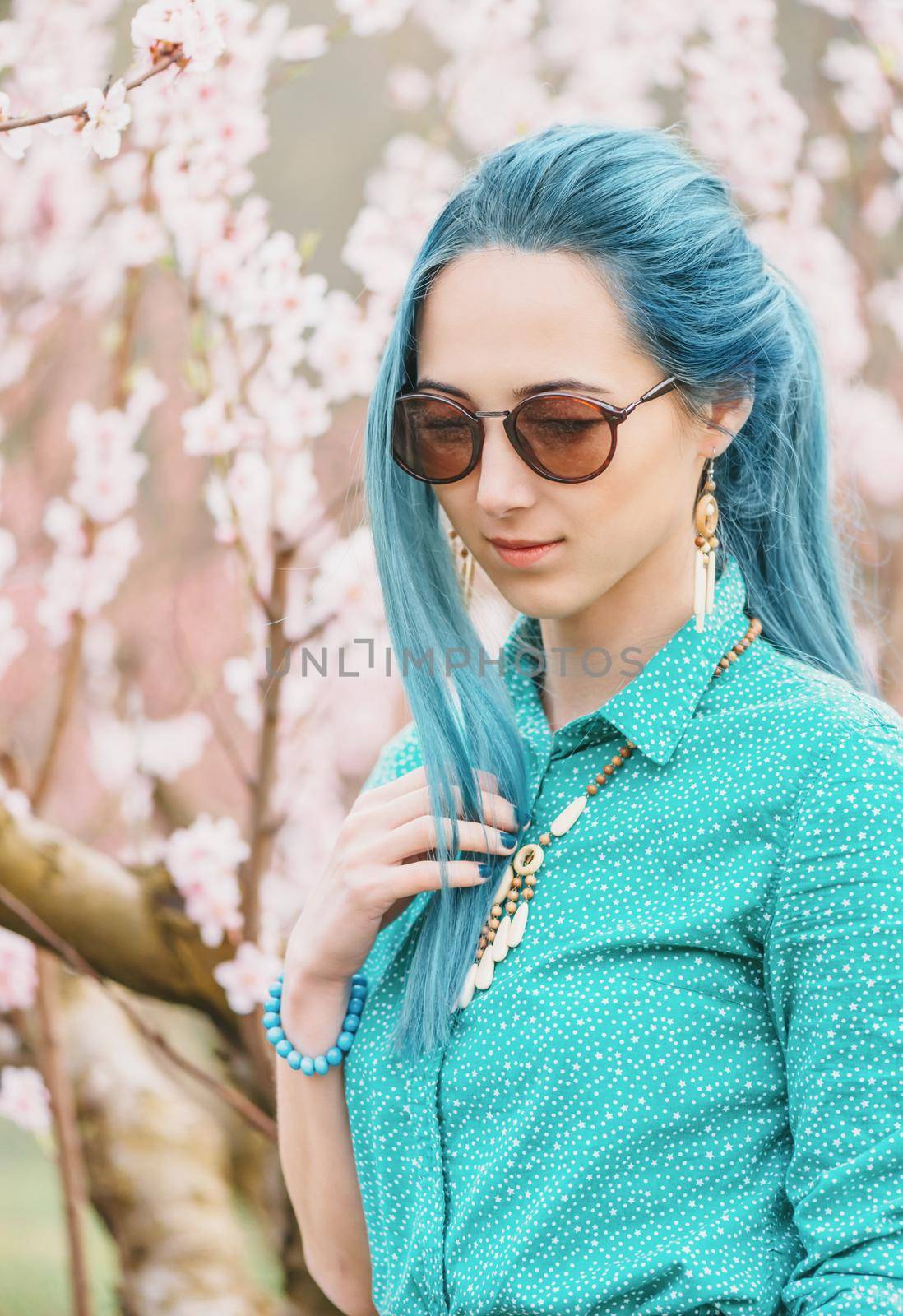 Beautiful young woman with blue hair walking in blossoming peach tree garden in spring.