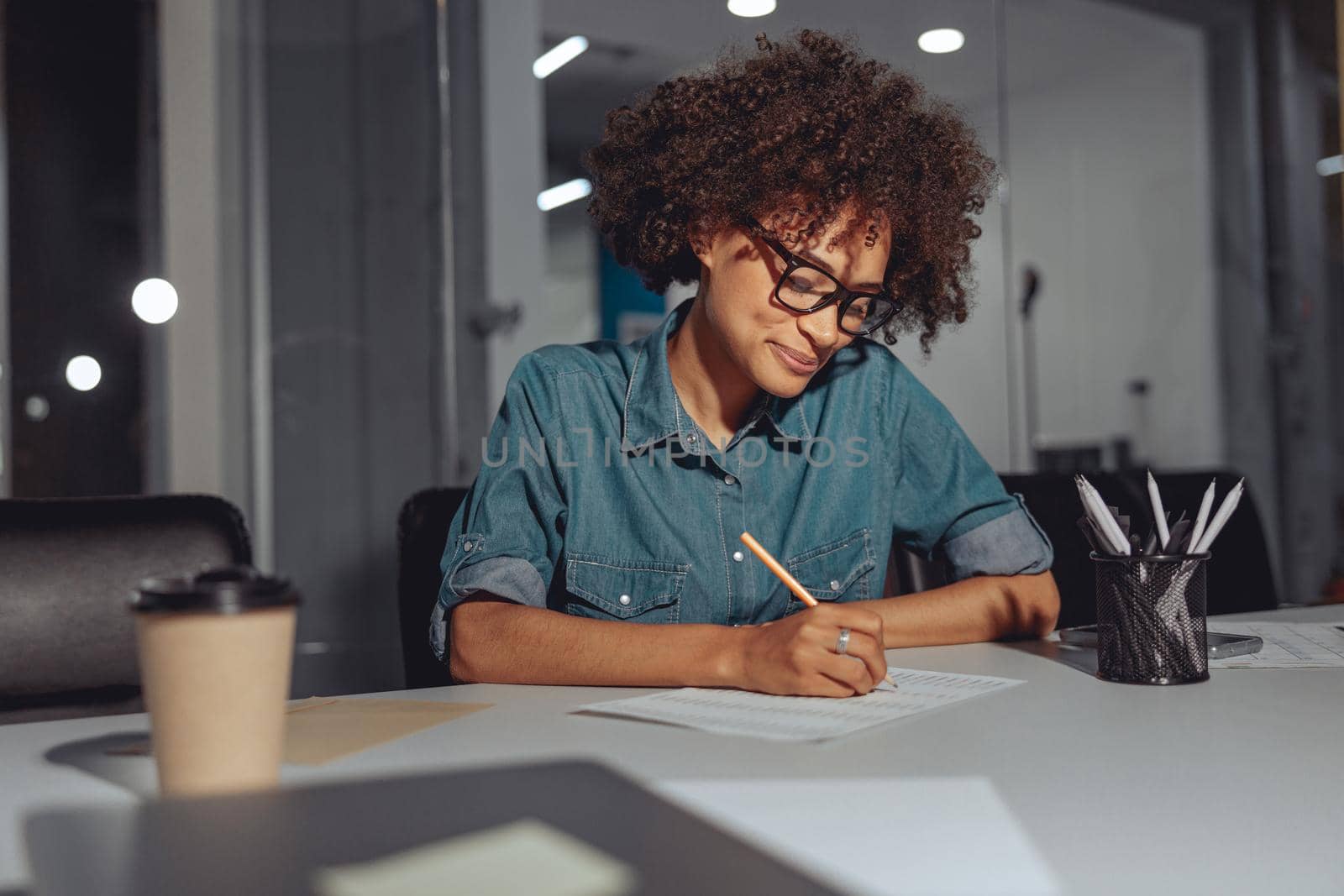 Happy Afro American lady sitting at the desk and writing on document while working in modern office