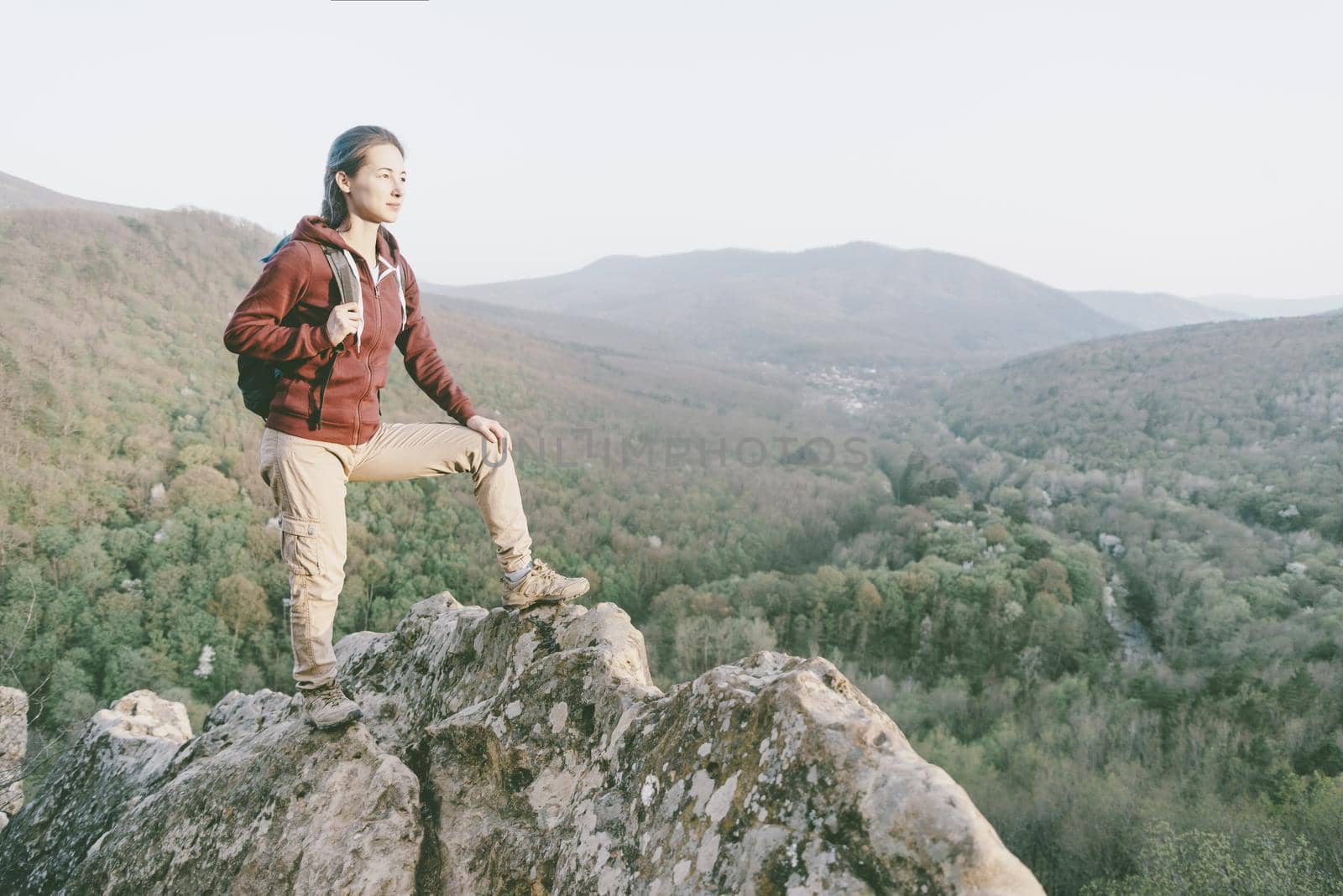 Traveler explorer girl with backpack standing on peak of cliff in the mountains and looking into the distance in summer