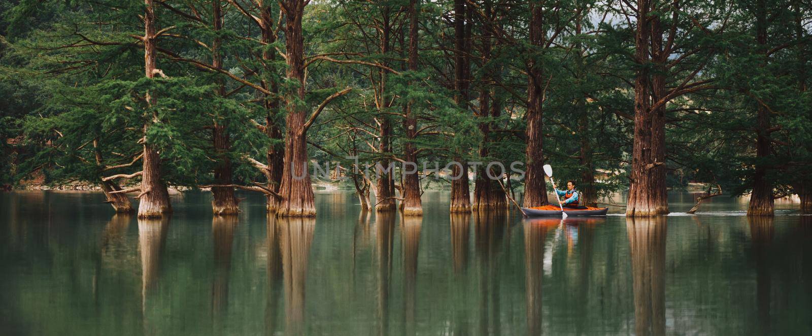 Explorer young man kayaking on lake on background of beautiful cypresses in summer, Anapa, Russia.