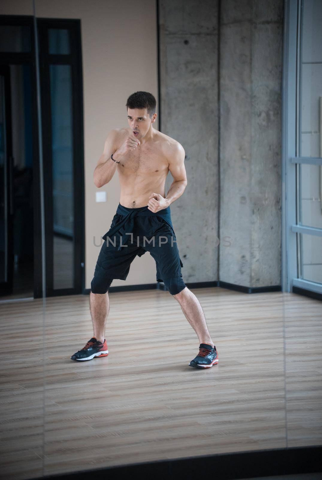 An athletic young man boxer standing in fighting pose in the bright studio. Mid shot