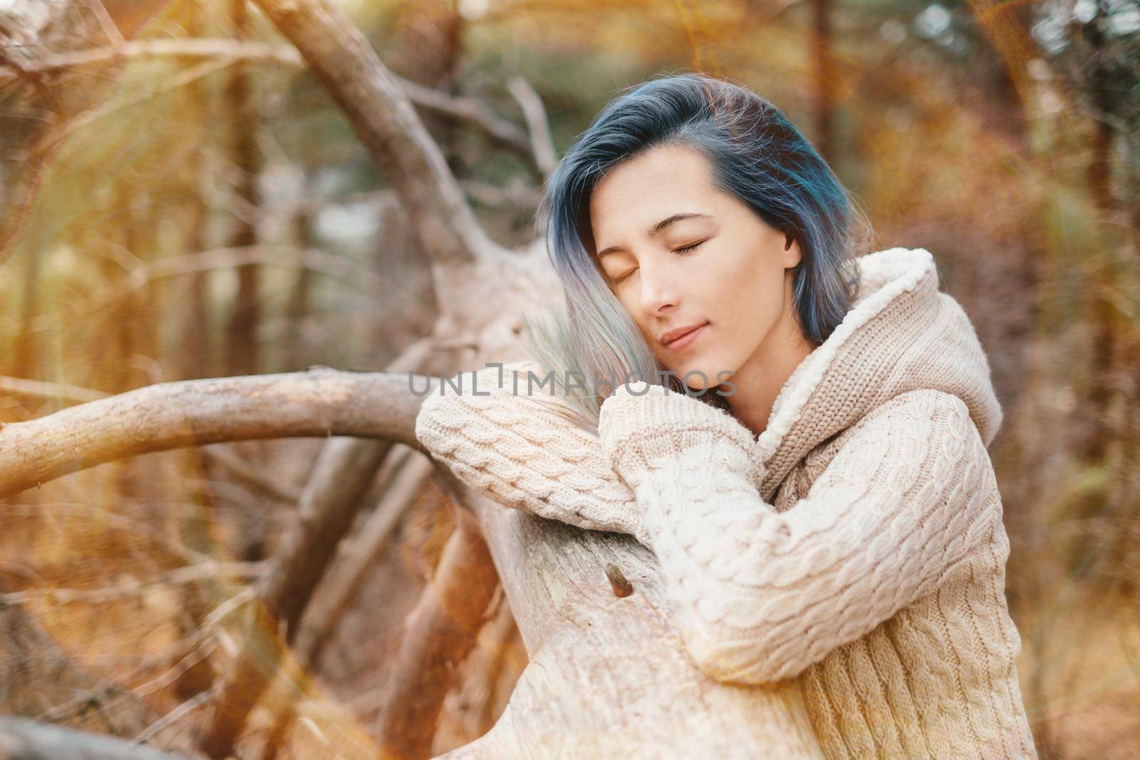 Beautiful young woman with blue hair standing with closed eyes near a tree at sunny day. Rest and relaxation outdoor. Image with sunlight effect.