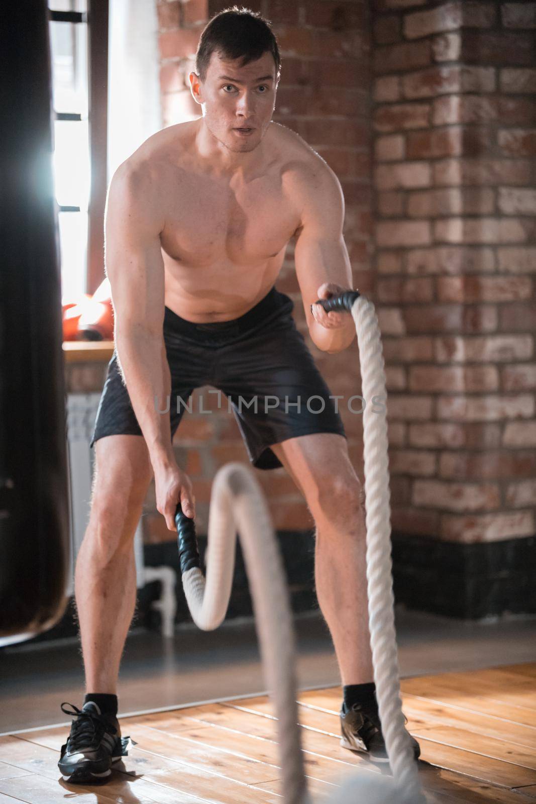 A concentrated man on training in the gym. Training his hands with ropes hitting on the floor. Mid shot
