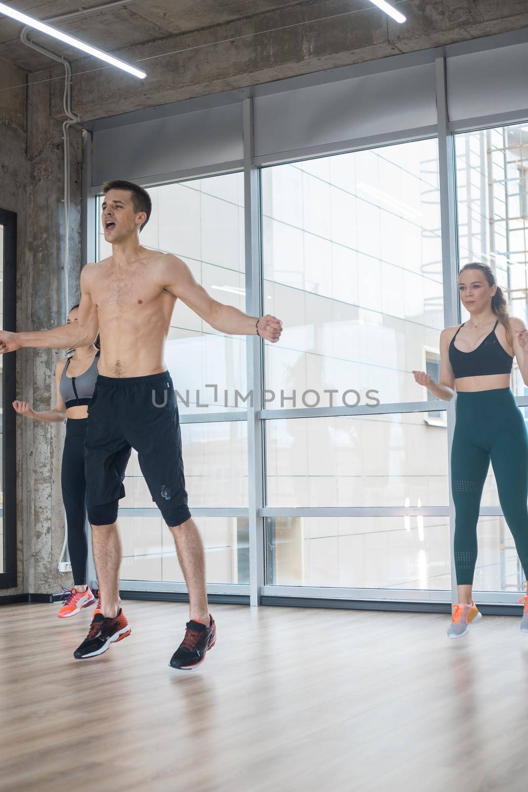 Fitness training in the bright studio - two young women training with their coach - jumping exercises. Mid shot