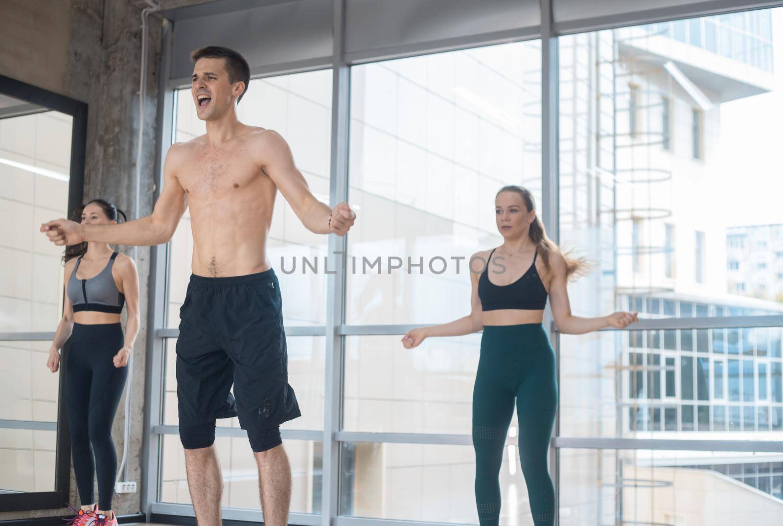 Fitness training in the studio - two young women training with their coach - jumping. Mid shot