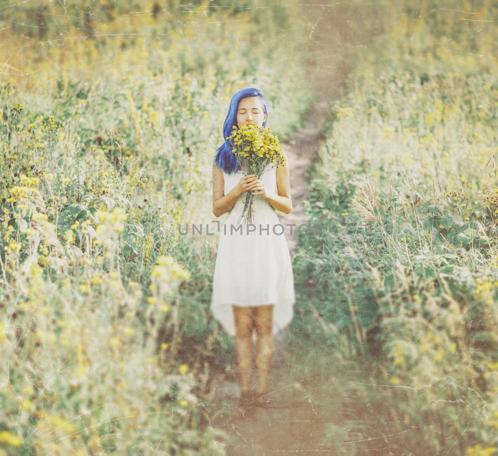 Beautiful young woman with blue hair and a bouquet of summer flowers standing in a field. Image with old textured effect.