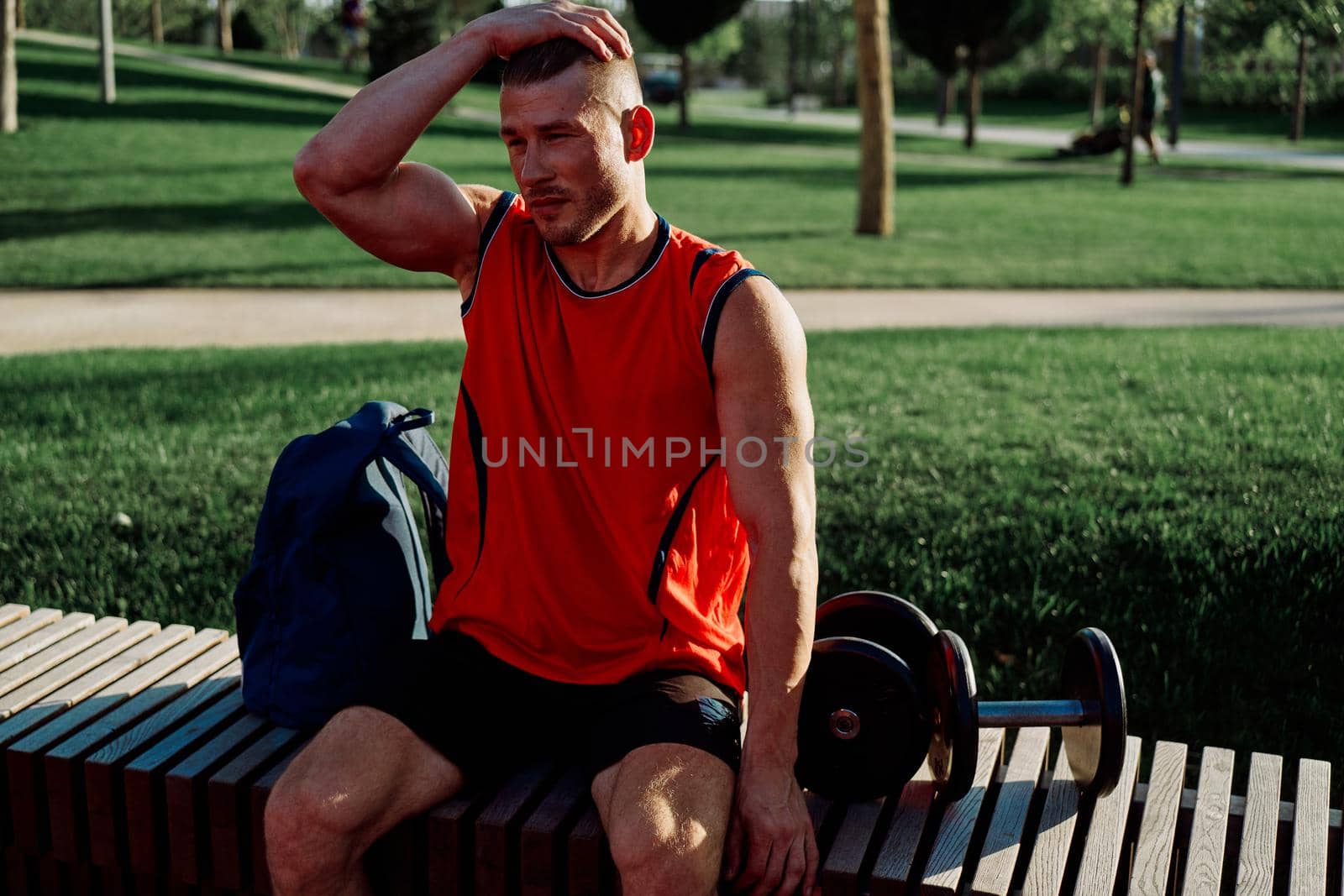 Cheerful male athlete in the park sits on a bench by Vichizh