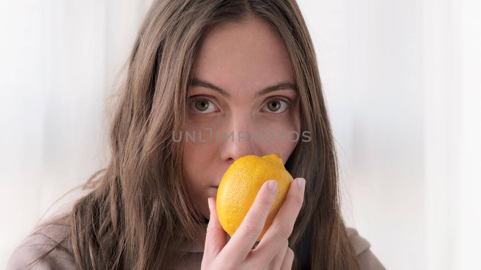 Woman sniffing lemon and does not smell due to illness shakes her head at home curtains