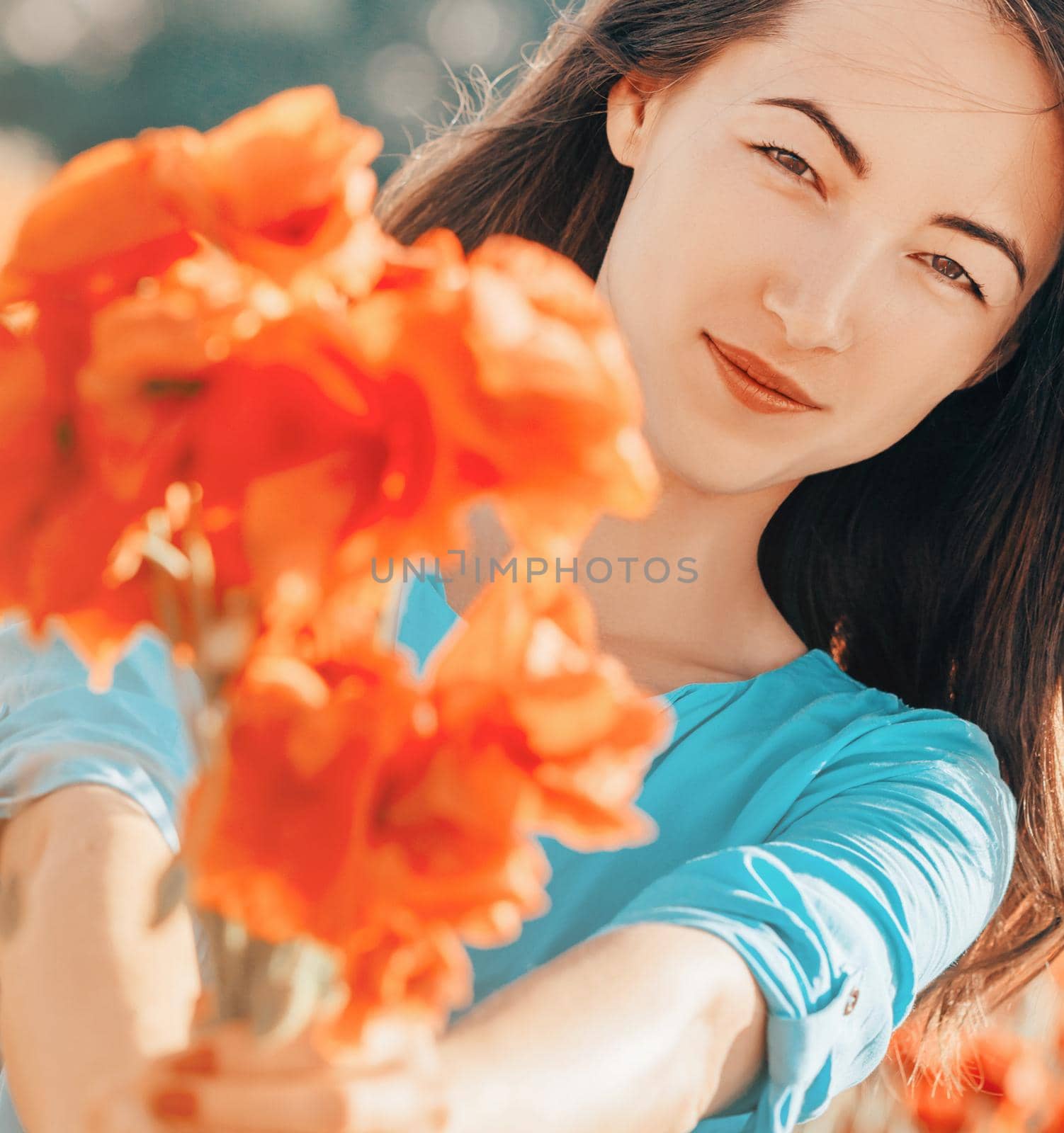 Outdoor portrait of smiling beautiful young woman giving a bouquet of poppies flowers, looking at camera.