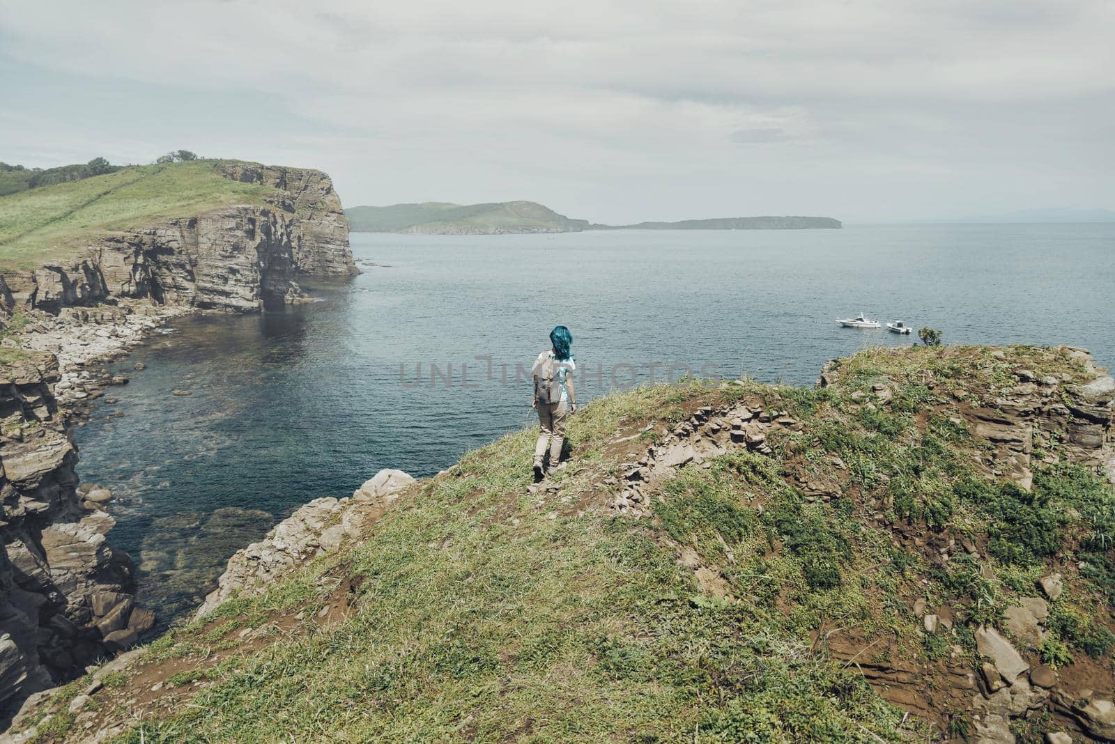 Traveler young woman with backpack walking on high cliff coast and enjoying view of sea.