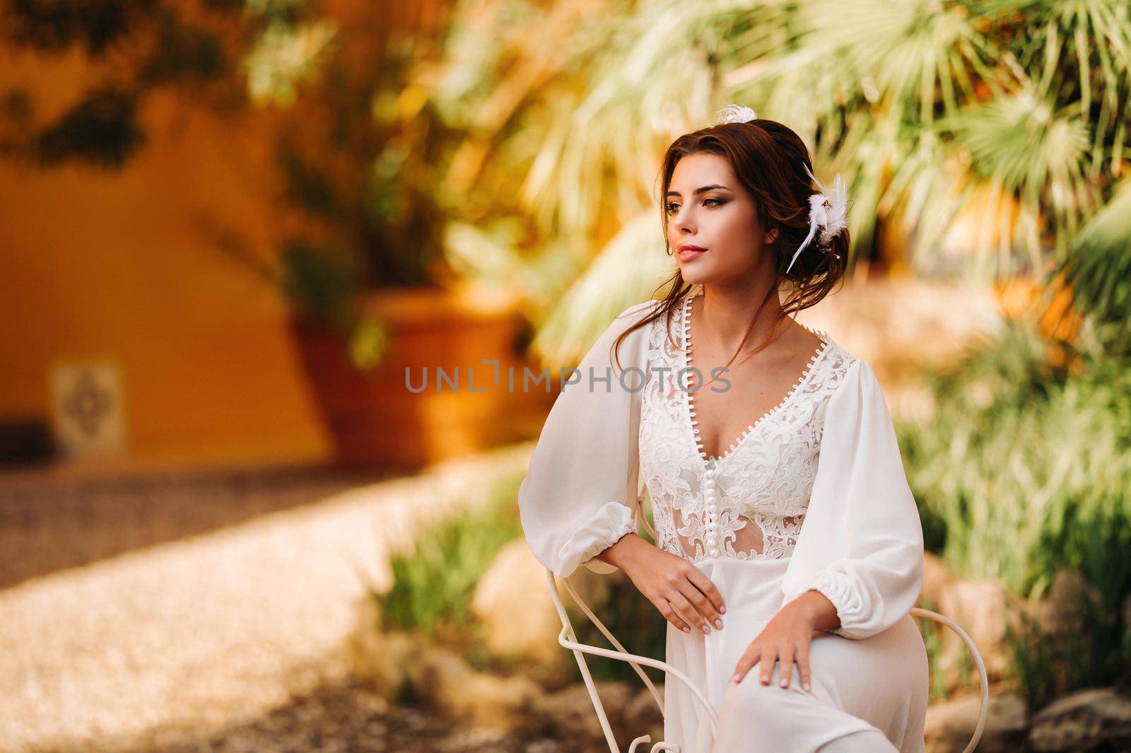 a beautiful bride is sitting on a chair and smiling in her underwear and dressing gown next to a Villa in Italy.morning of the bride in Tuscany.