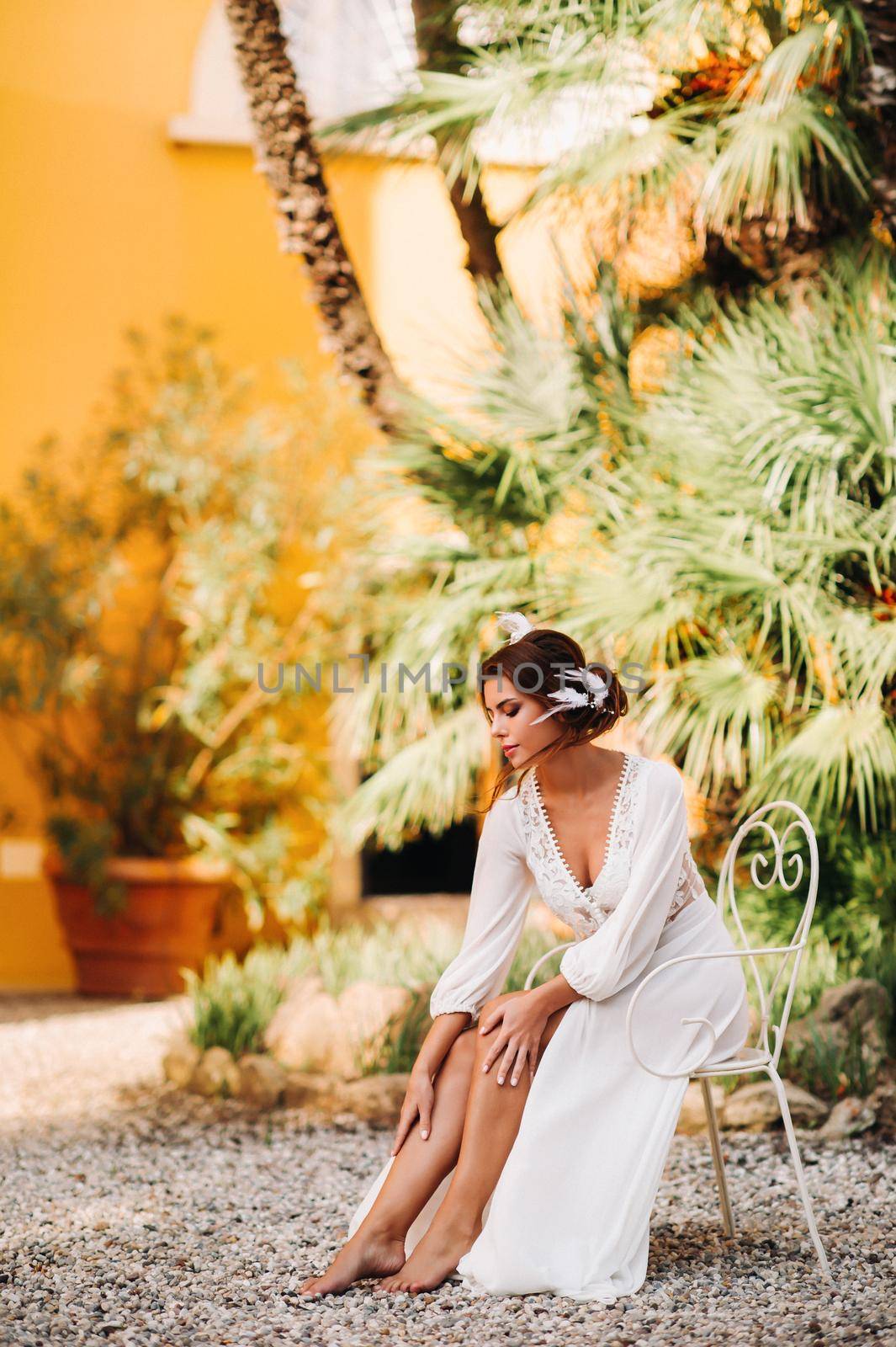 a beautiful bride is sitting on a chair and smiling in her underwear and dressing gown next to a Villa in Italy.morning of the bride in Tuscany by Lobachad