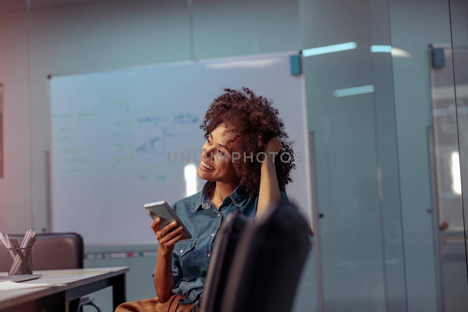 Smiling young lady using mobile phone in the office by Yaroslav_astakhov