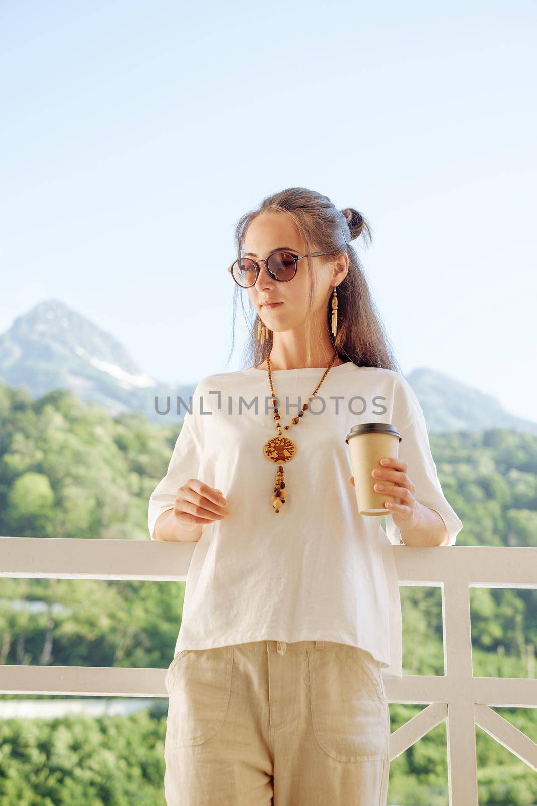 Beautiful woman resting with cup of coffee on balcony in front of mountains. by alexAleksei