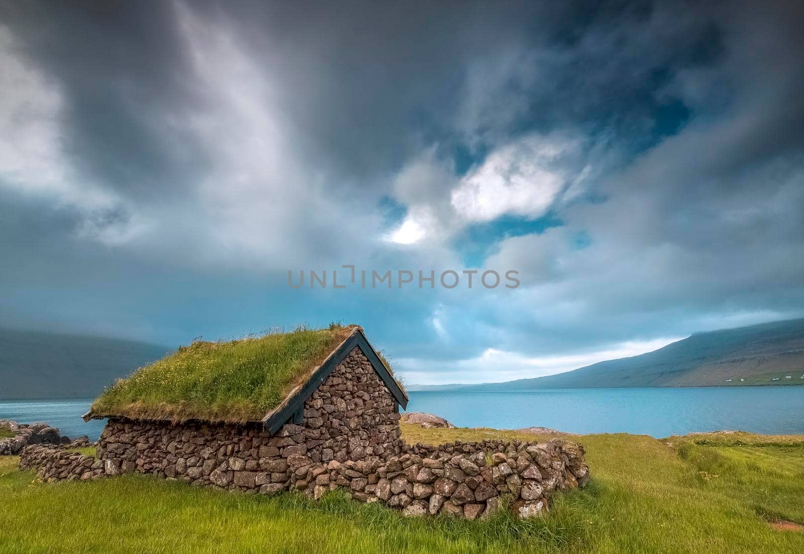 Small house near a blue lake, a small house made of stones with covered grass on the shore of a beautiful lake by isaiphoto