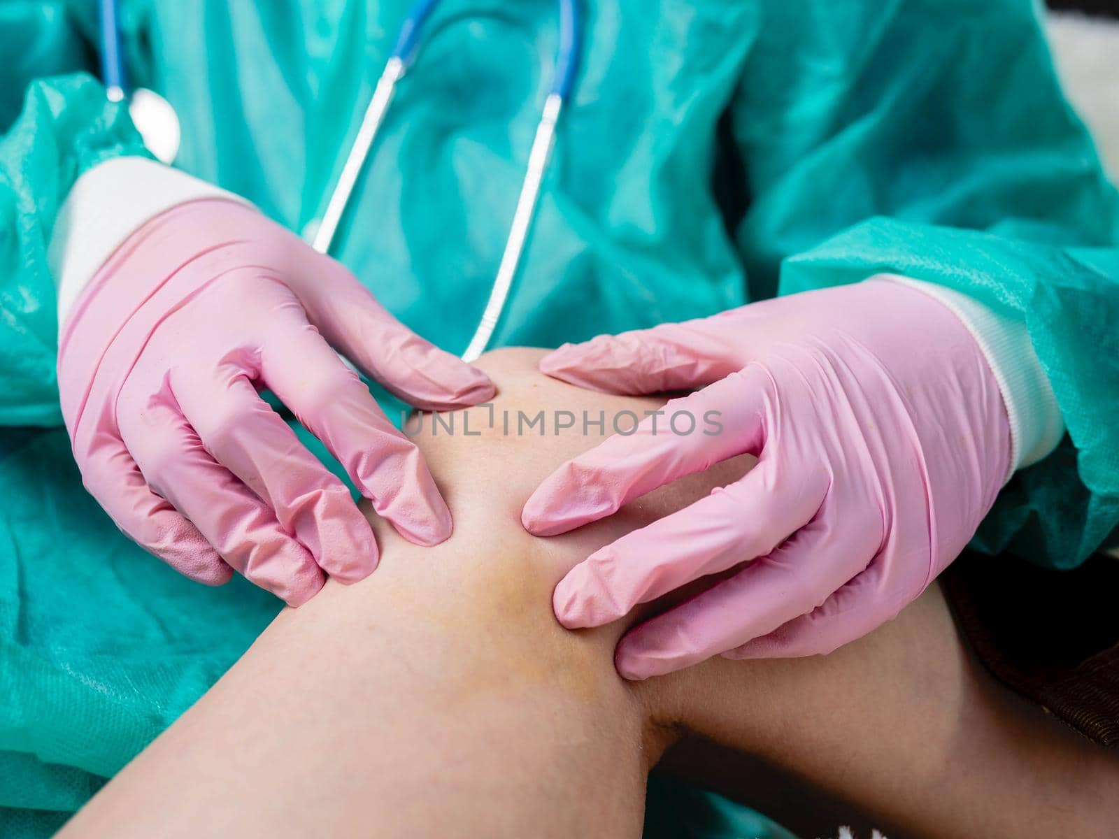 A traumatologist wearing medical gloves palpates the injured knee during a routine examination of the patient. by Utlanov