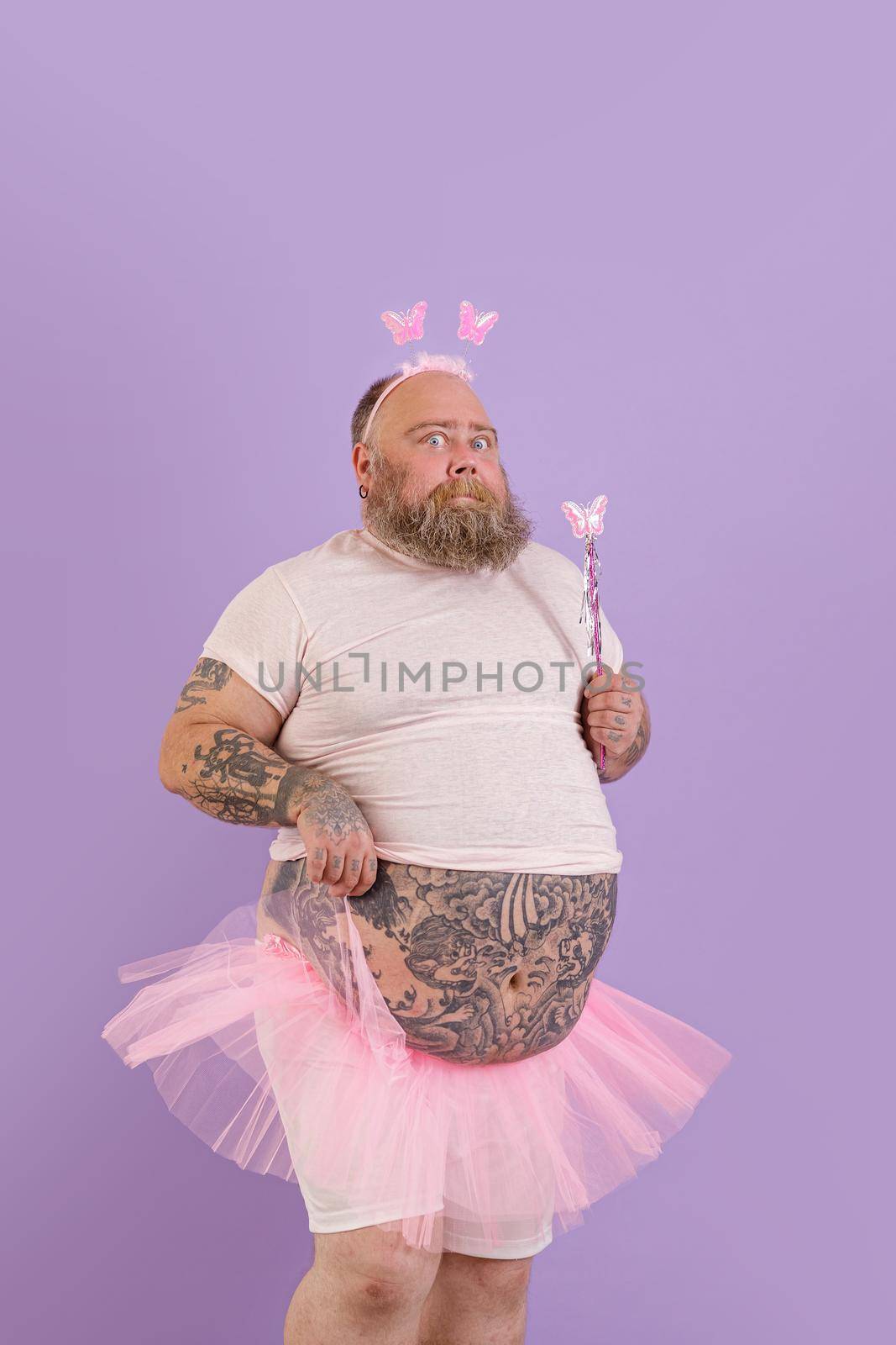 Expressive middle aged man with overweight wearing fairy suit poses on purple background by Yaroslav_astakhov