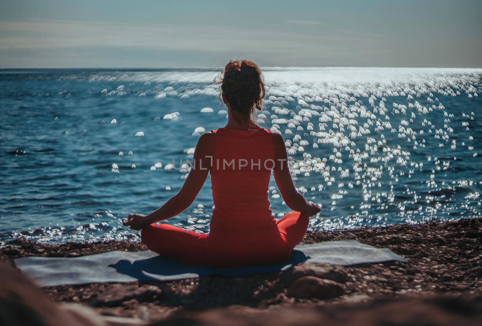 Selective focus. Young beautiful caucasian woman in a red suit practicing yoga on the beach at sunrise near the sea. Yoga. Healthy lifestyle. Meditation concept. by panophotograph