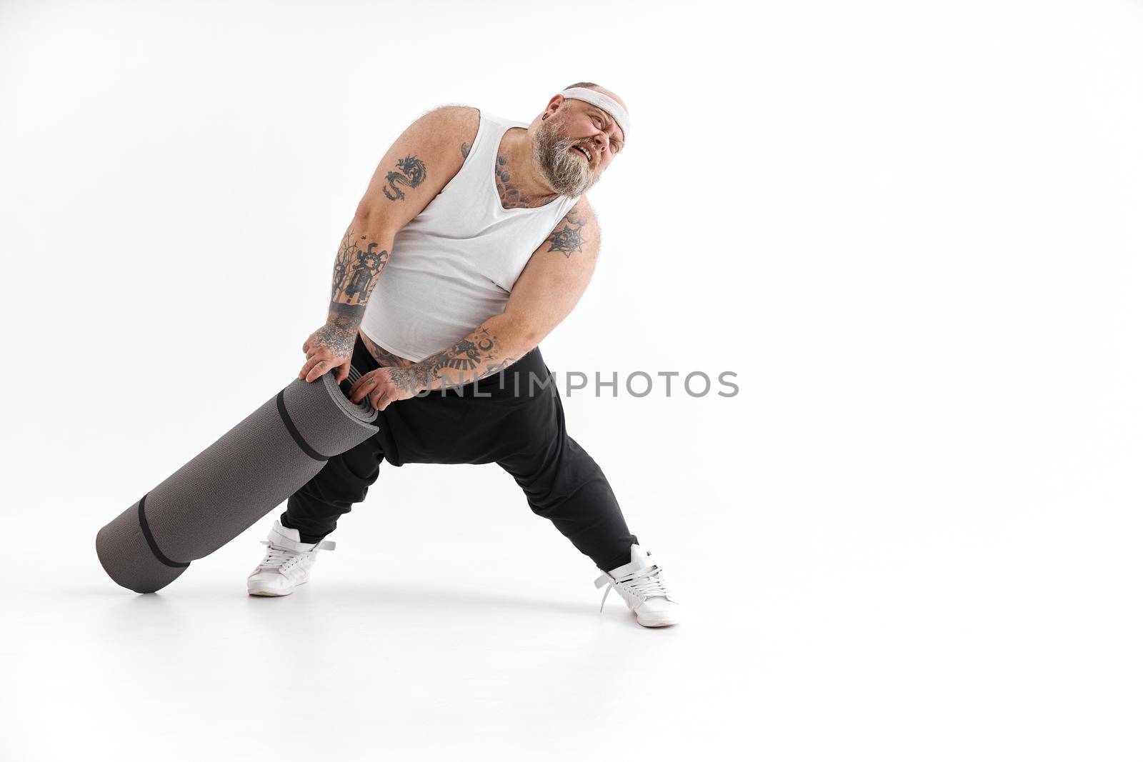 Happy fat man with big belly and tattos in sports wear with exercise mat