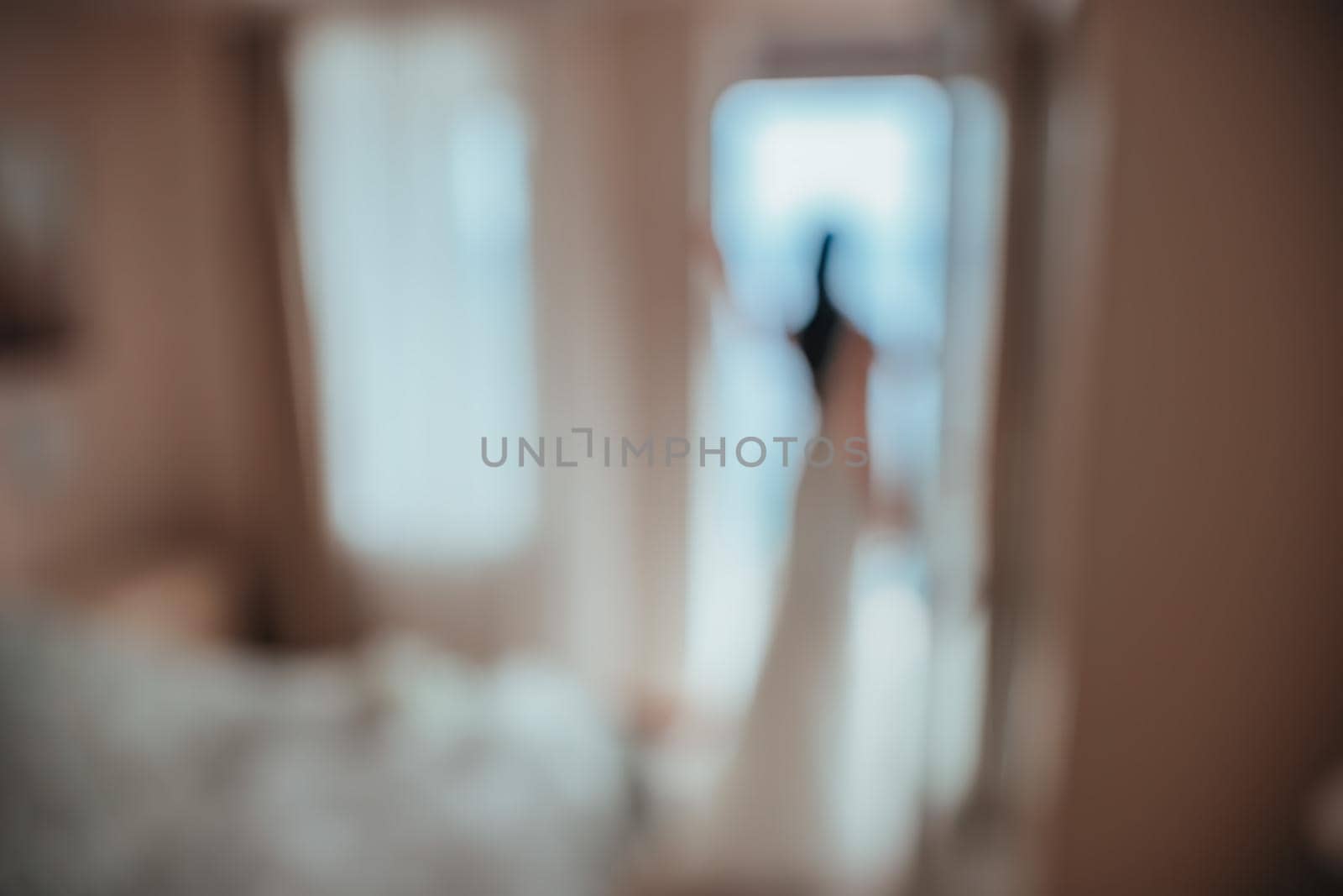 Blurred image for the background. Back view of beautiful brunette bride young woman in the white lace dress near window in the hotel room. Wedding concept
