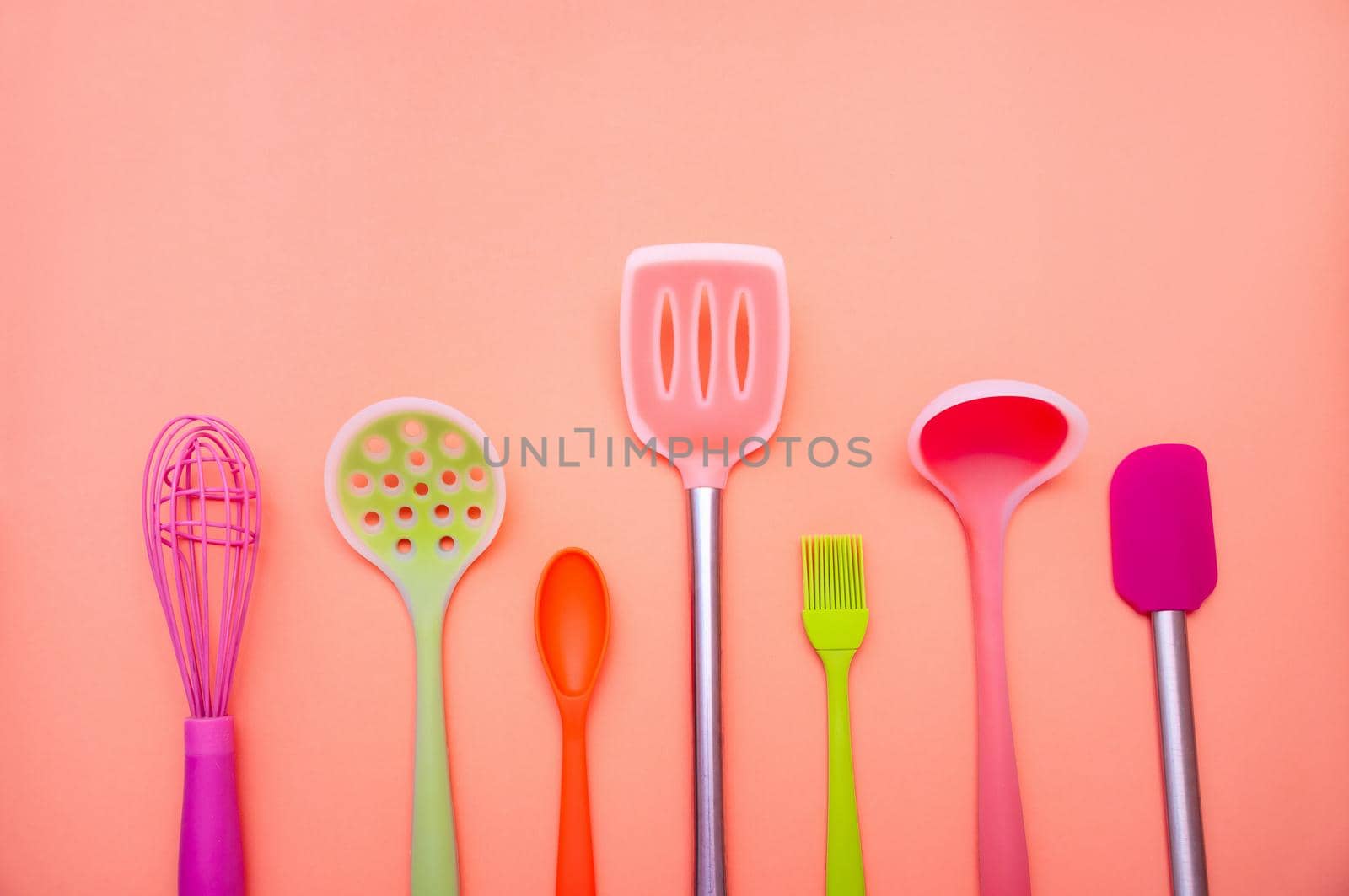 Various Colored Silicone Kitchen Utensils on Coral Background. Copy Space For Your Text.