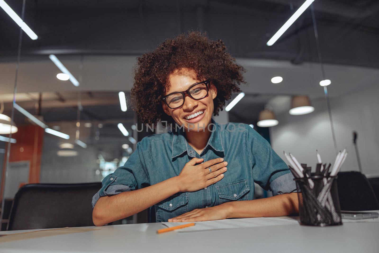 Happy pretty lady sitting at work desk and showing gestures in modern office