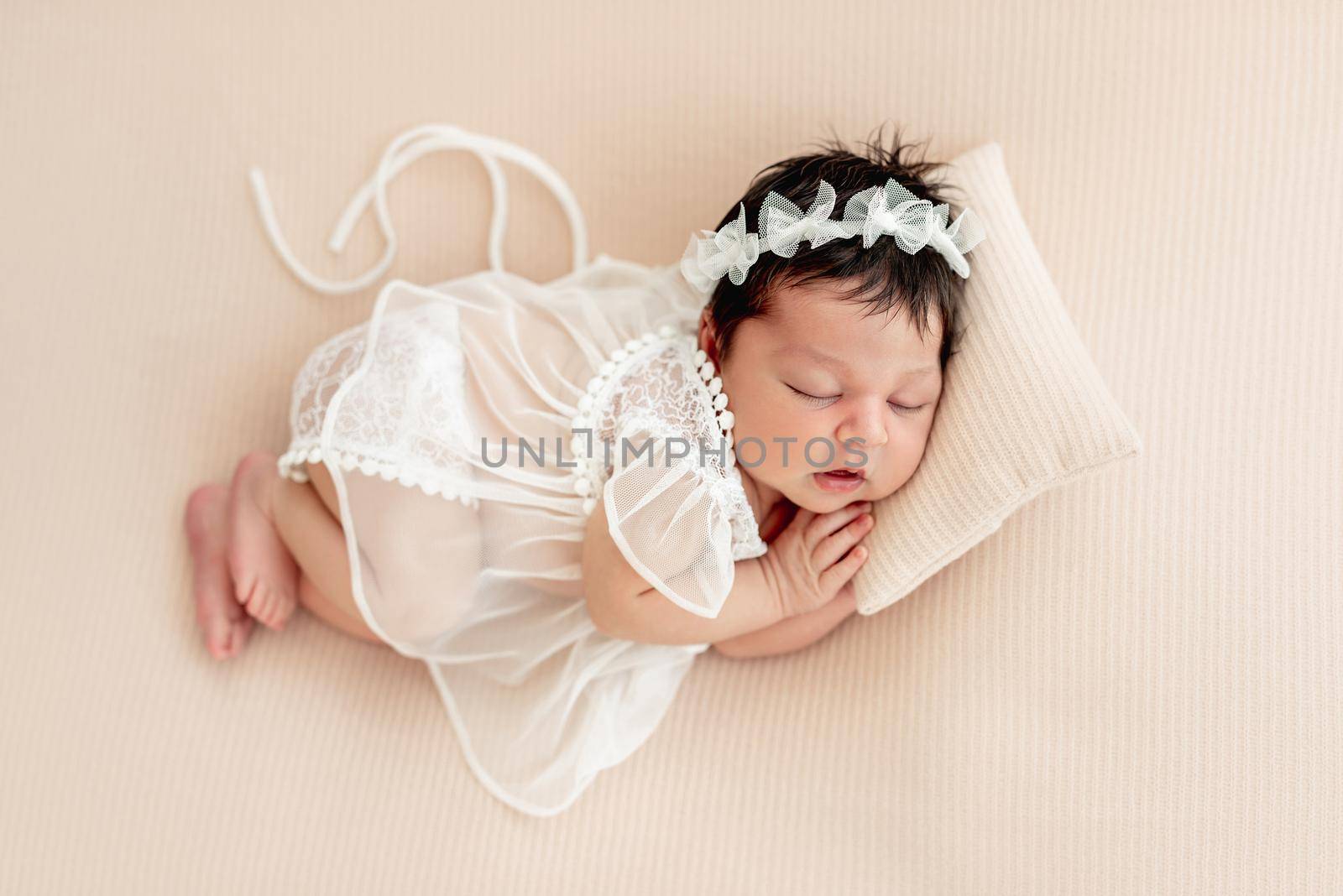 Cute newborn in lace dress sleeping on side with tiny pillow