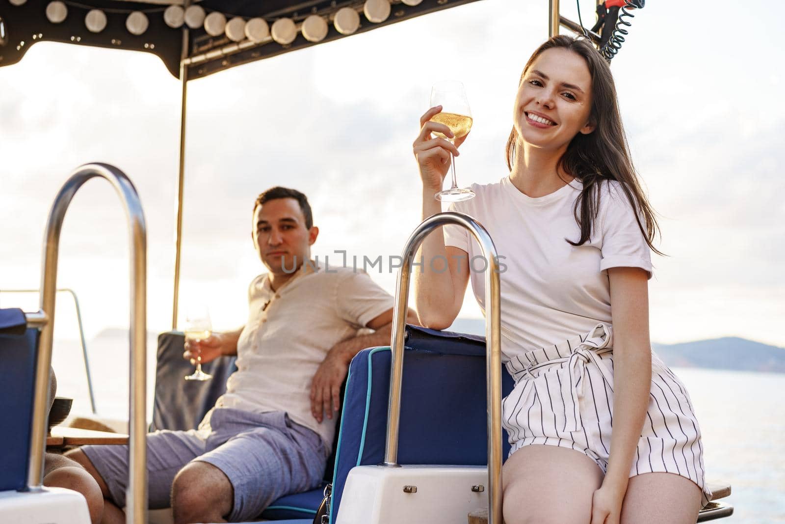 Young loving couple sitting on the yacht deck and drinking wine together