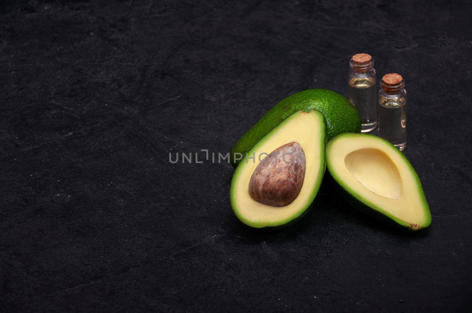 Ripe Half Avocados with Oil on Dark Stone Background. Copy Space For Your Text.