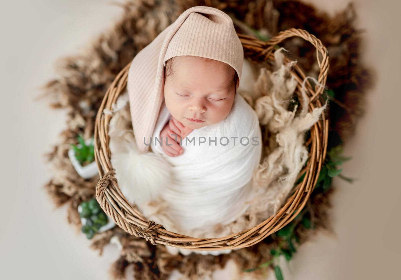 Cute newborn in hat with big balabon sleeping in basket