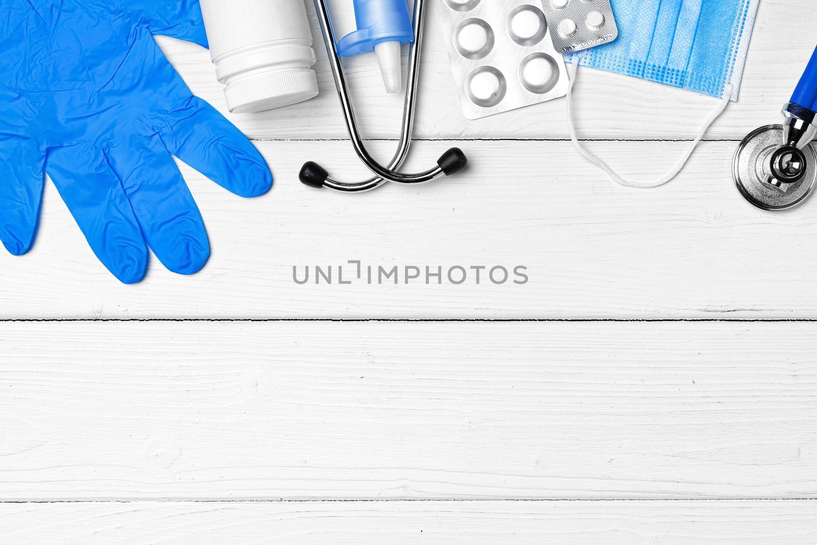 Medical equipment. Stethoscope, mask and pills on white wooden desk close up