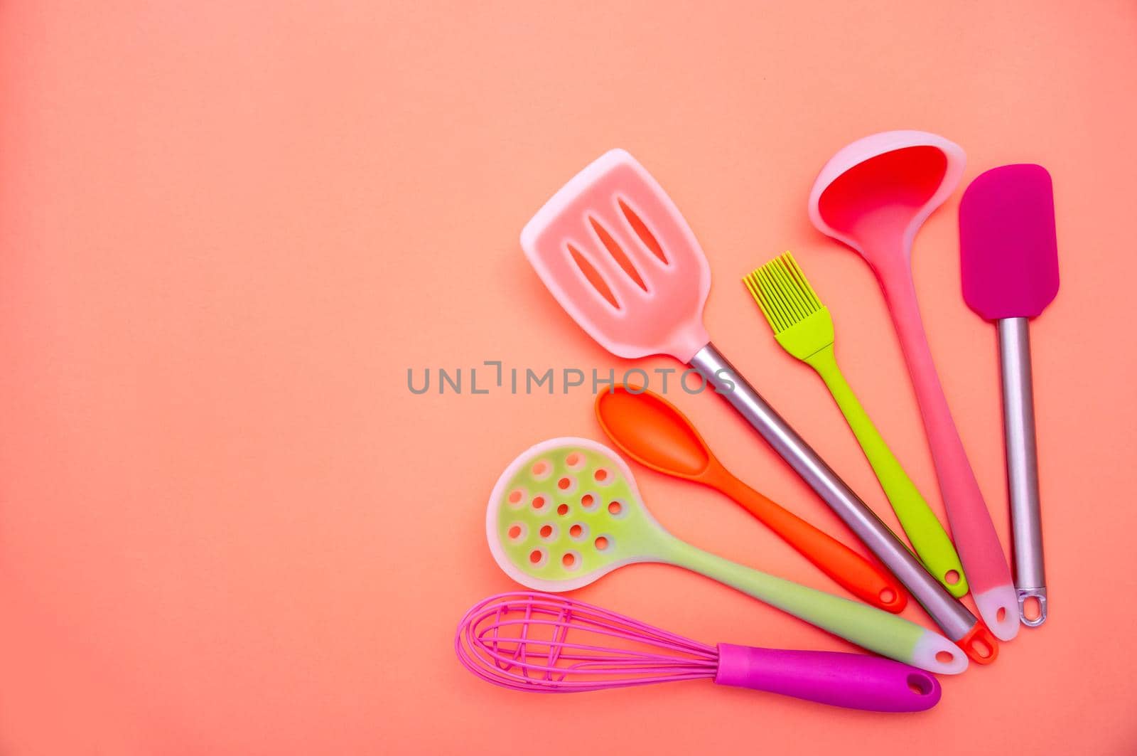 Various Colored Silicone Kitchen Utensils on Coral Background. Copy Space For Your Text.