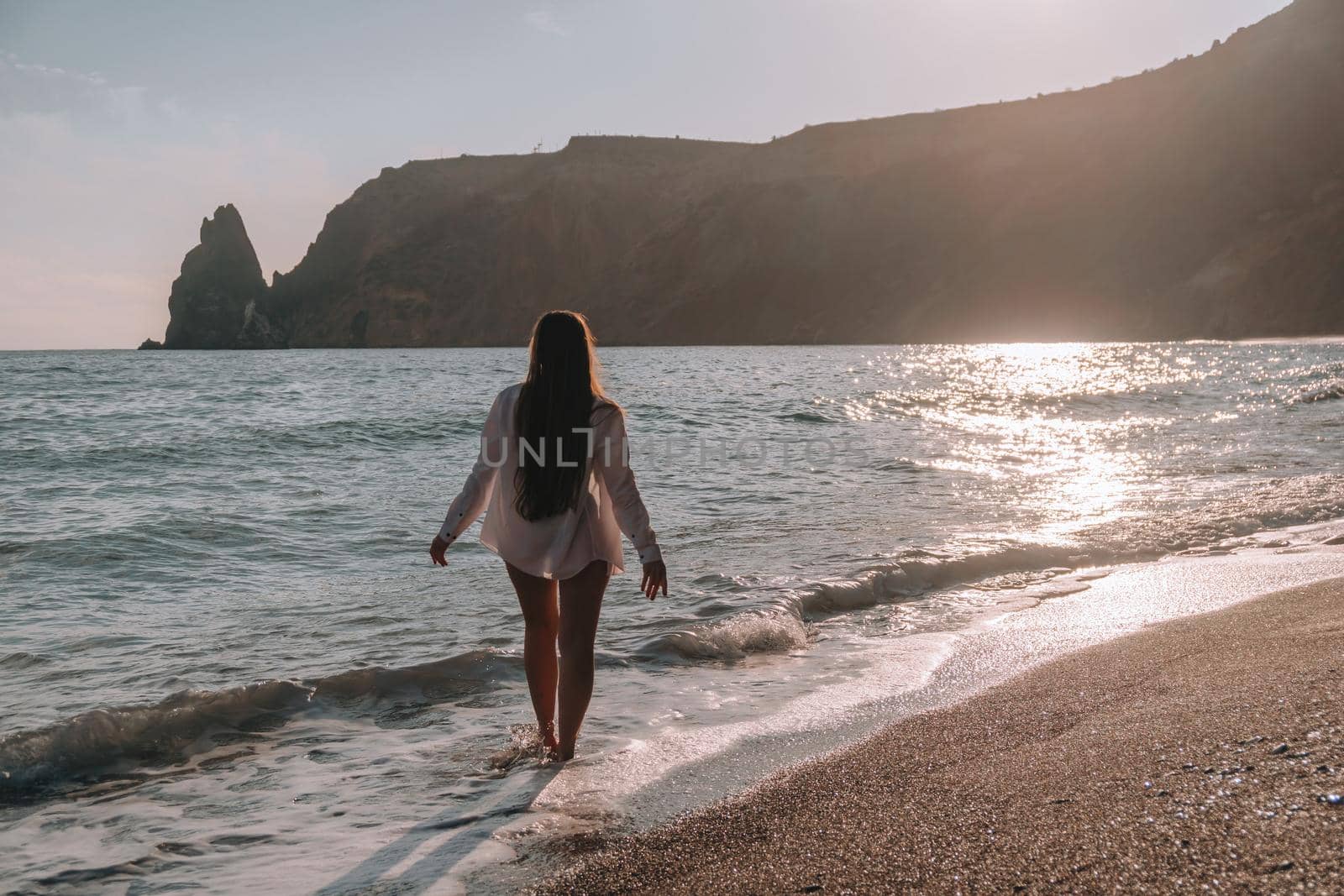 Selective focus. Happy carefree sensual woman with long hair in black swimwear posing at sunset beach. Silhouette of young beautiful playful positive woman outdoor. Summer vacation and trip concept.