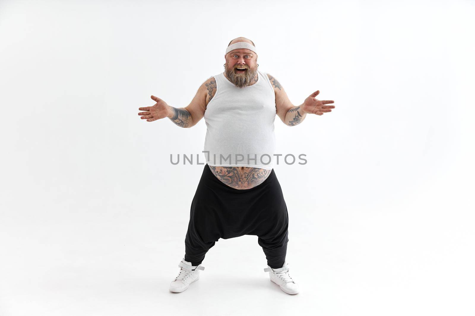 Happy fat man with big belly and tattoes in sports wear posing on white background