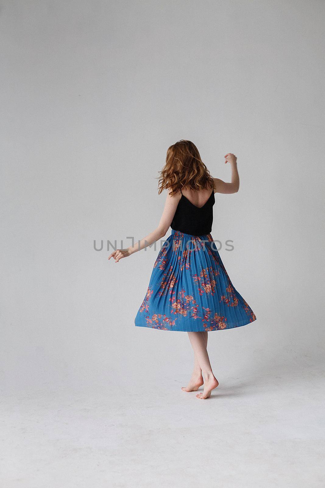 pretty woman in blue skirt with bare feet spinning around on white background. dancing movements of young lady, indoors portrait. caucasian skinny female with long brown hair dances on cyclorama